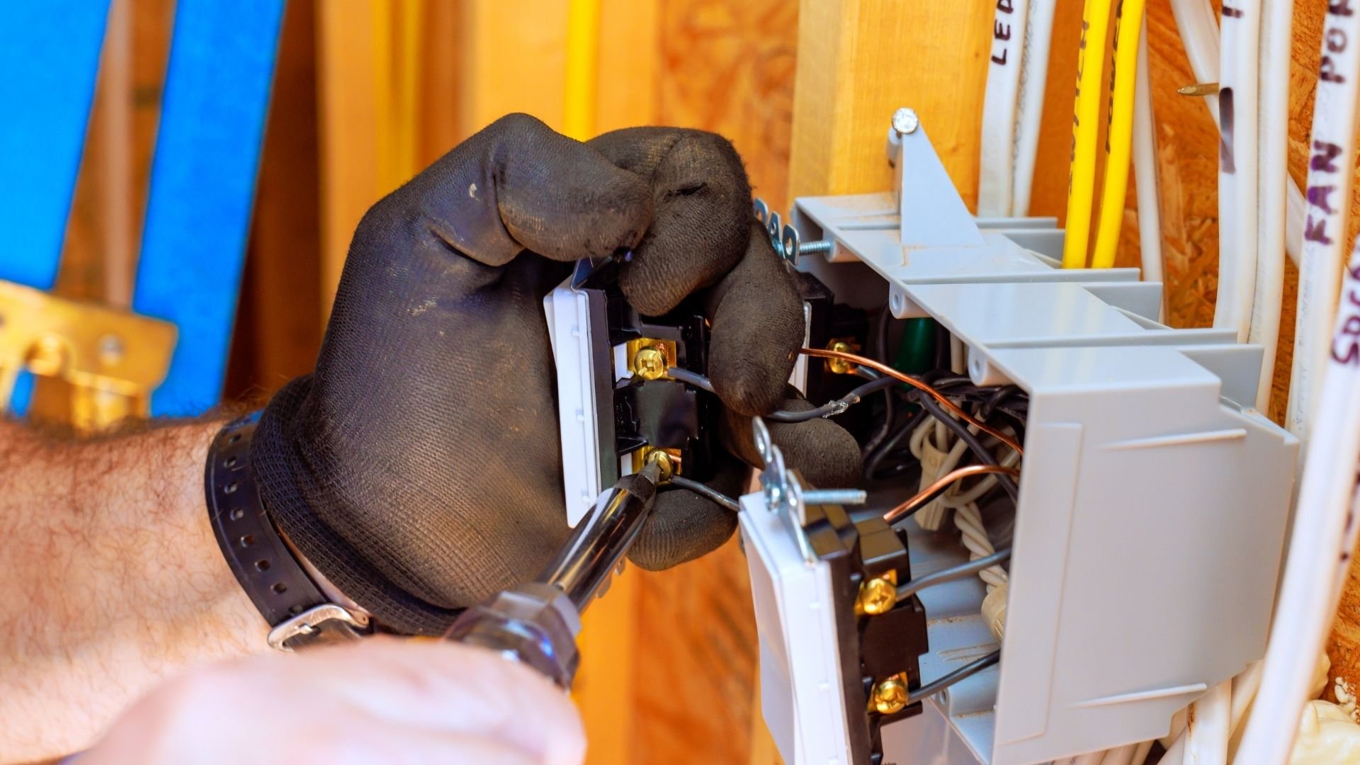 Gloved hand performing electrical work on circuit breaker panel with yellow background
